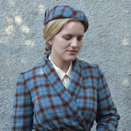 A woman with blonde hair wearing a jacket and matching berret made from Cygnet Tartan, designed by Vicki Taiwo