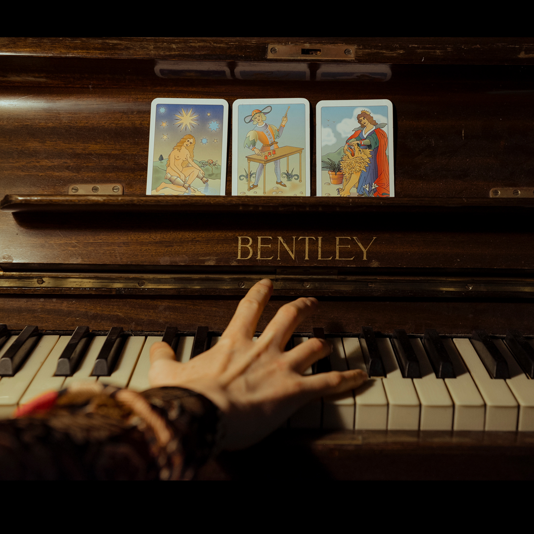 A dark image of someone's right hand on a piano. Instead of sheet music, there are tarot cards.