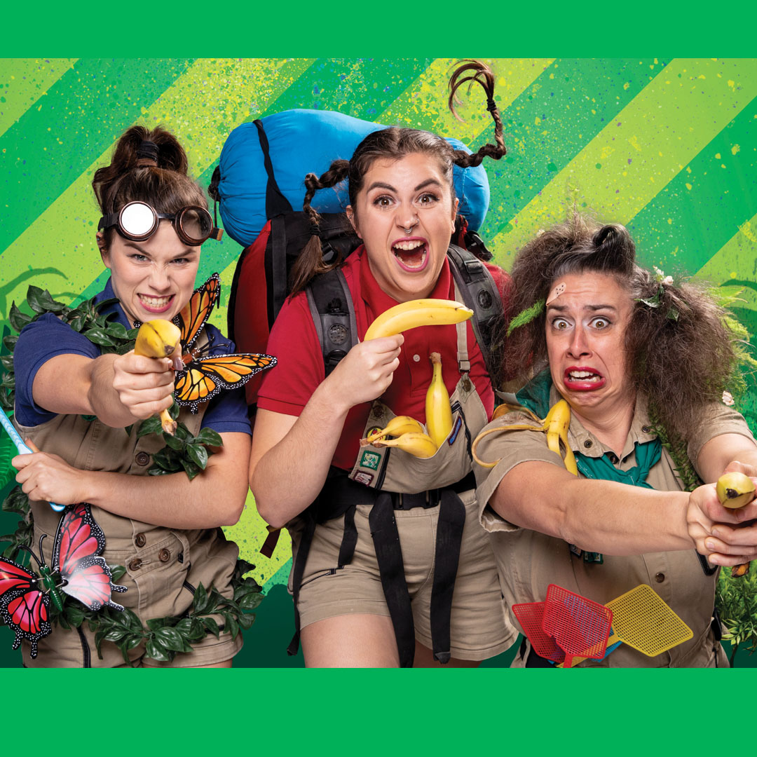 Three women wielding bananas as guns pointed towards the camera. They are child-like adventure-looking people with very animated expressions on their faces.