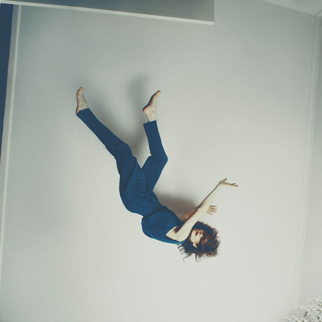 A woman looks to be frozen on the ceiling. She wears blue clothing and has brown hair. Her face is partially hidden by her hair.