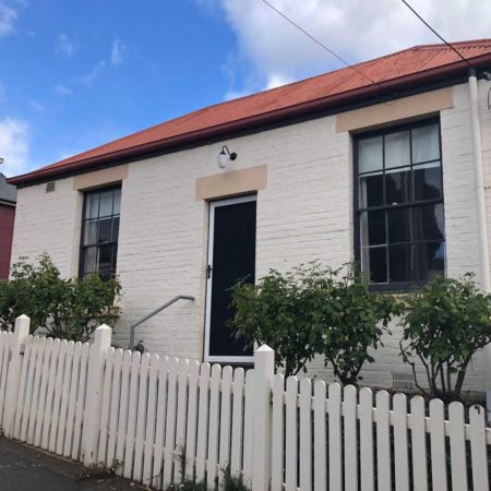 Photo of a white Georgian Cottage, with a white picket fence at the front.