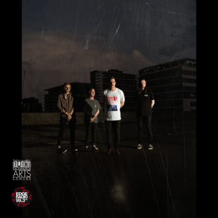 A group of four white men stand in the darkness. We see them from a distance.