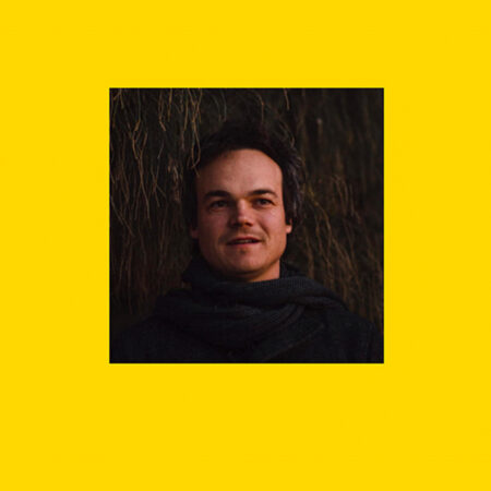 An image of Chris Coleman sits on a yellow background. He is a white male with dark brown hair.