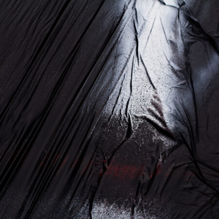 A dark image of light shining down on a wrinkled, black fabric surface.