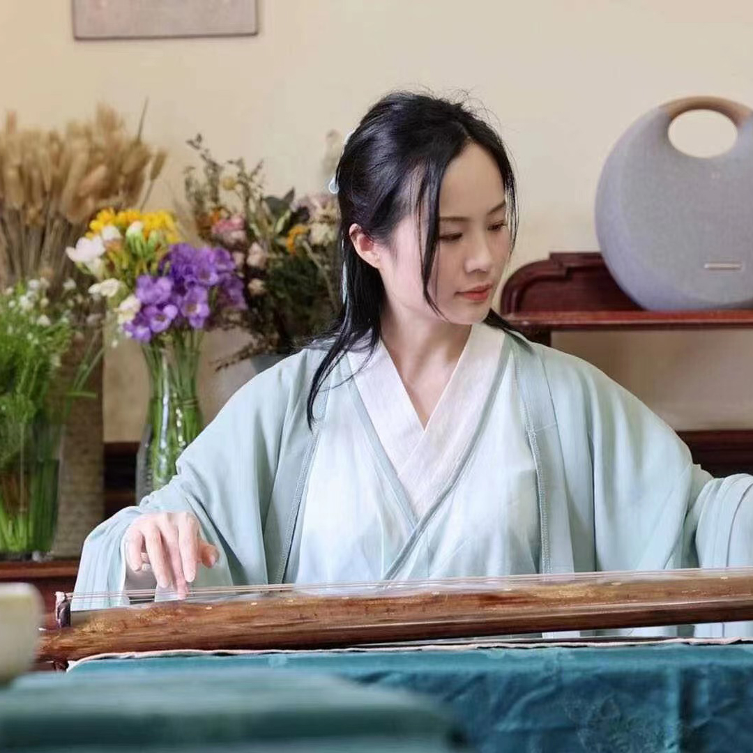 A Chinese woman sits at a table preparing a tea ceremony.