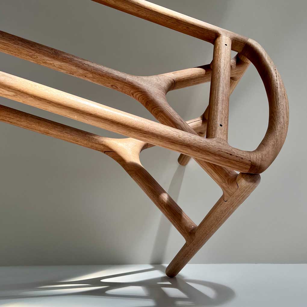 A wooden bench made from Tasmanian oak, against a white background. The legs of the bench are casting shadows against the wall and floor.