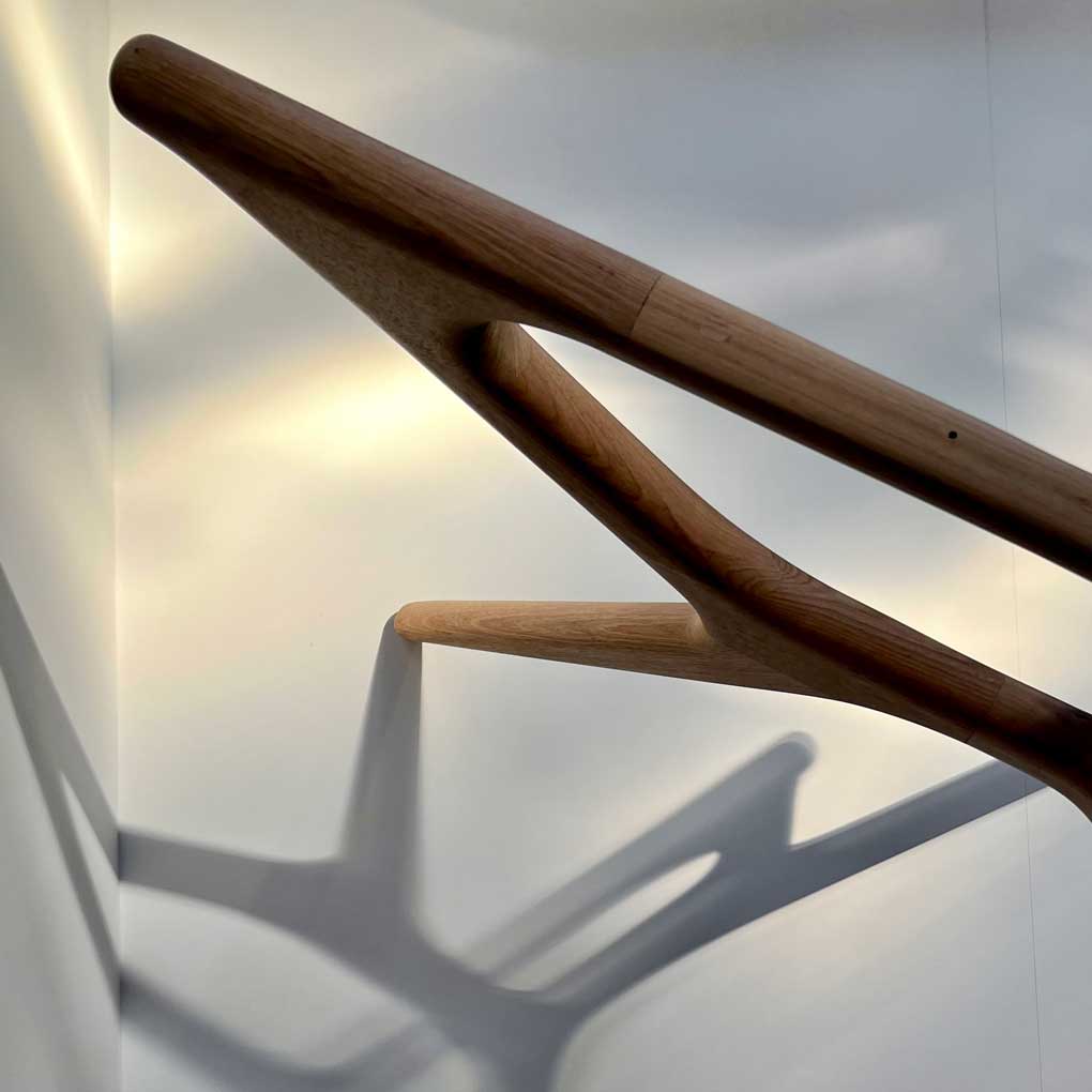 A close up of the legs of a dining table made from Tasmanian oak, against a white background. The legs are casting shadows against the wall and floor.