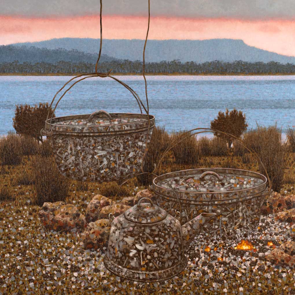 Two rusted metal cooking pots and a rusted metal kettle cit amongst stones and tufts of grass on the foreshore of a river. In the background the ky is pink from the sunset above the mountain range.