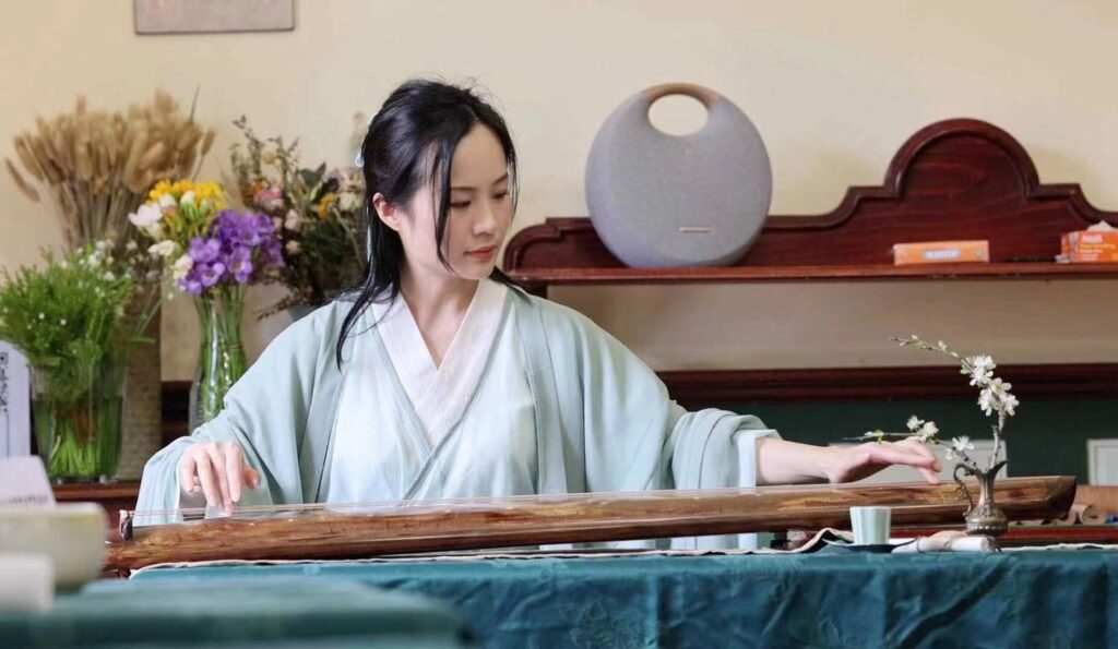 A Chinese woman sits at a table preparing a tea ceremony. 