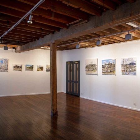 Photograph of the Sidespace Gallery : A room with white walls and dark wooden floor. A support beam is in the middle of the room. To the far end of the room is a wooden french door.