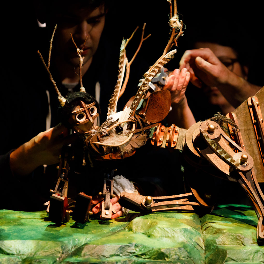 Image of a man and horse puppets made of small wooden pieces and scraps including feathers, bolts and leather. Two puppeteers hold the puppets.