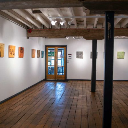 Photograph of the Top Gallery : A room with white walls and dark wooden floor. Two support beams are in the middle of the room. To the far end of the room is a wooden, french multi-paned door.