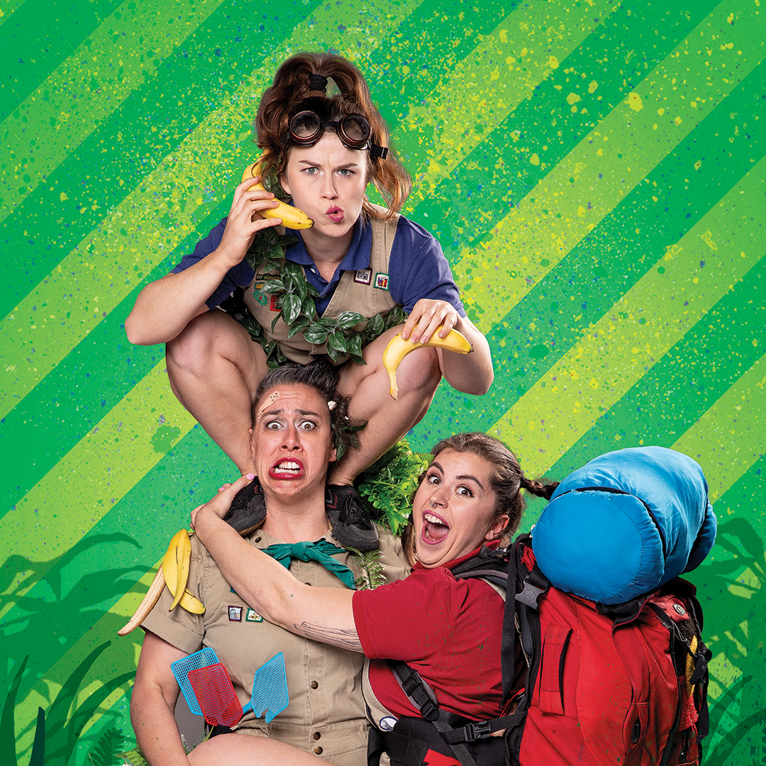 Three women pulling funny faces, one on the others shoulders and one clinging to another sit on a bright green striped background. they wear childlike clothing and one carries a blue backpack.
