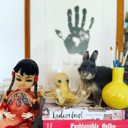 Image of a china doll, glass octopus, furry rabbit, yellow vase, and books on a shelf