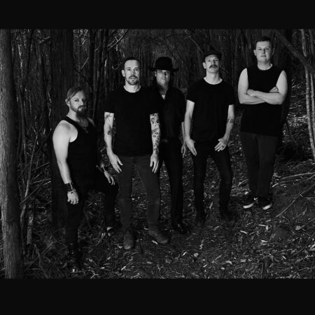 A group of 5 people wearing black stand in a forest. The image is black and white and they all look directly to camera.