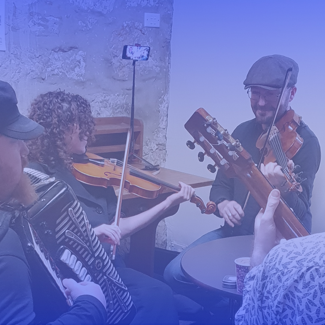 A group of musicians play in a circle. They are all male and white. They play in an indoor area.