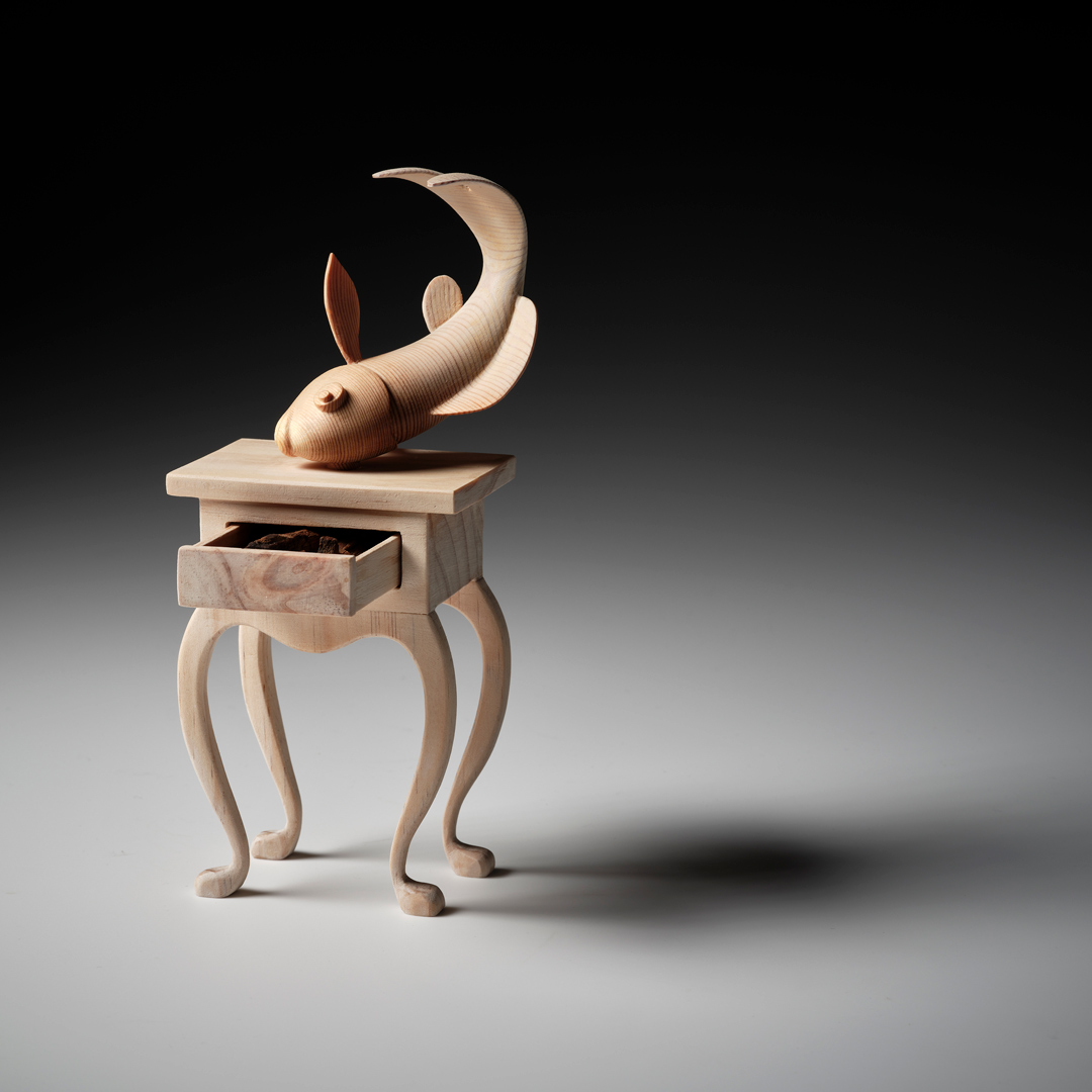 A whimsical wooden carving of a carp balancing on a delicate table with curved wooden legs.